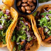 Taco Trio · Three soft shell street style tacos topped with onions, cilantro salsa and your choice of me...