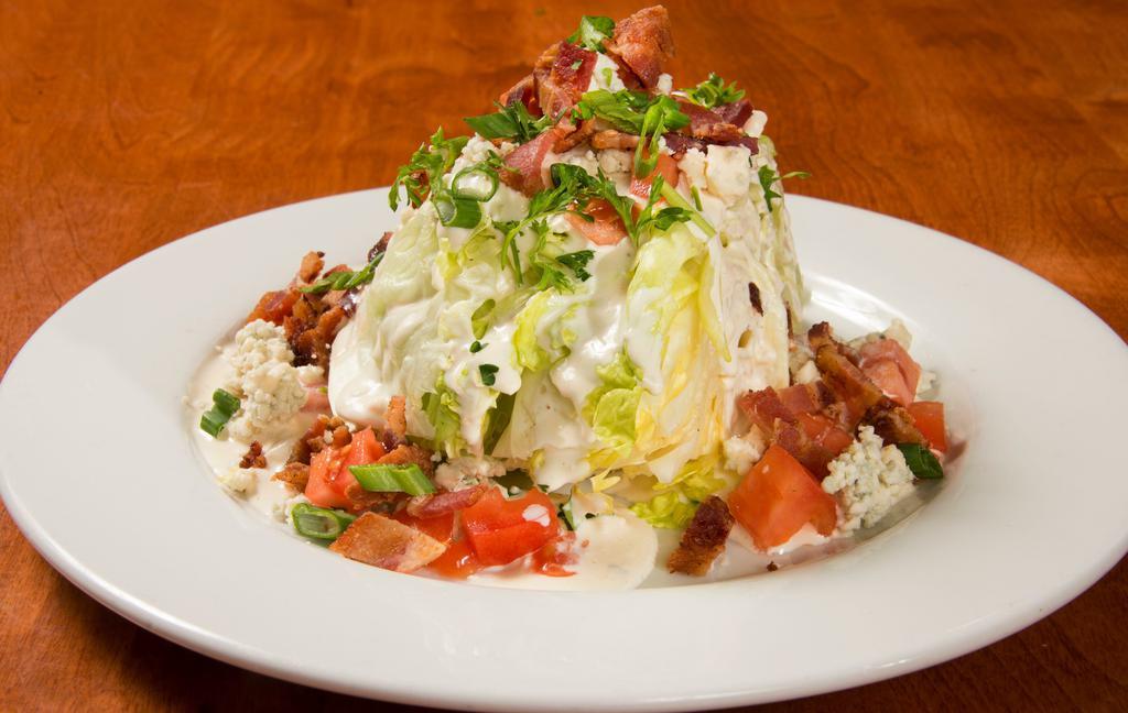 The Classic Iceberg Wedge · A wedge of iceberg lettuce topped with blue cheese dressing, extra blue cheese crumbles, chopped bacon, tomatoes, green onion, and parsley.