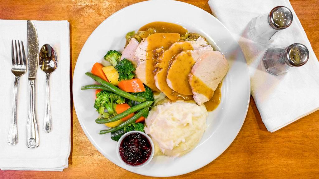 All American Turkey Dinner · Hand carved slow roasted turkey breast topped with gravy, served with a cornbread sage stuffing, real garlic mashed potatoes, fresh vegetables, and cranberry sauce.