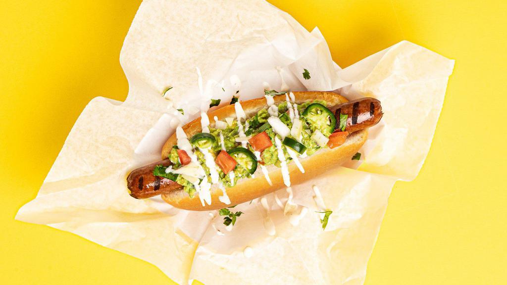 Chihuahua Dog · Hot dog topped with guacamole, sliced jalapenos, tomatoes, and a sour cream drizzle, served on a fluffy bun.