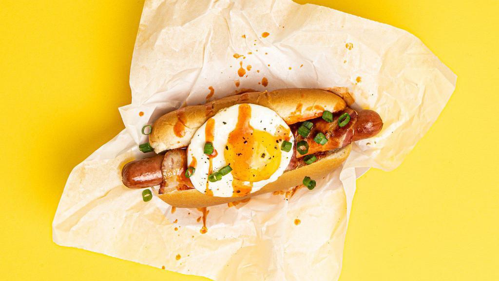 Morning Dog · Bacon wrapped dog topped with a fried egg, sliced scallions, and drizzled with sriracha, served on a fluffy bun.