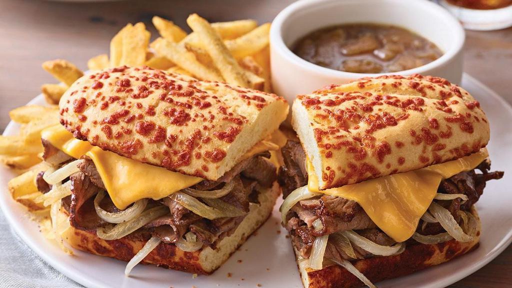 The Prime Rib Dipper · Thinly sliced prime rib topped with grilled onions and melted American cheese. Served on a toasted Cheddar roll with our house-made herb mayo and French onion Au jus for delectable dipping.  Served with classic fries.