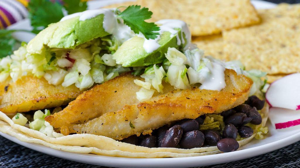 Fish Taco · Pan-seared fish with chopped cabbage, avocado, black beans, cilantro rice and Mexican cream on top of a soft corn tortilla as a taco. Served with chips.