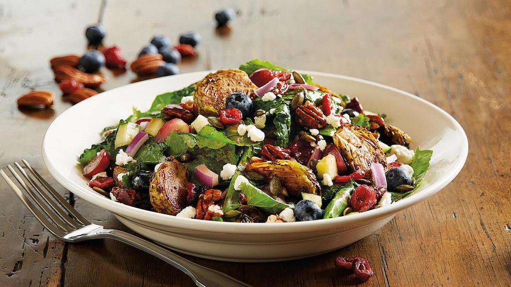 Enlightened Kale And Roasted Brussels Sprouts Salad · Baby kale | roasted brussels sprouts | romaine | fresh blueberries | sweet red grapes | dried cranberries | goat cheese crumbles | cucumbers | candied pecans | toasted pepitas | red onions | strawberry vinaigrette