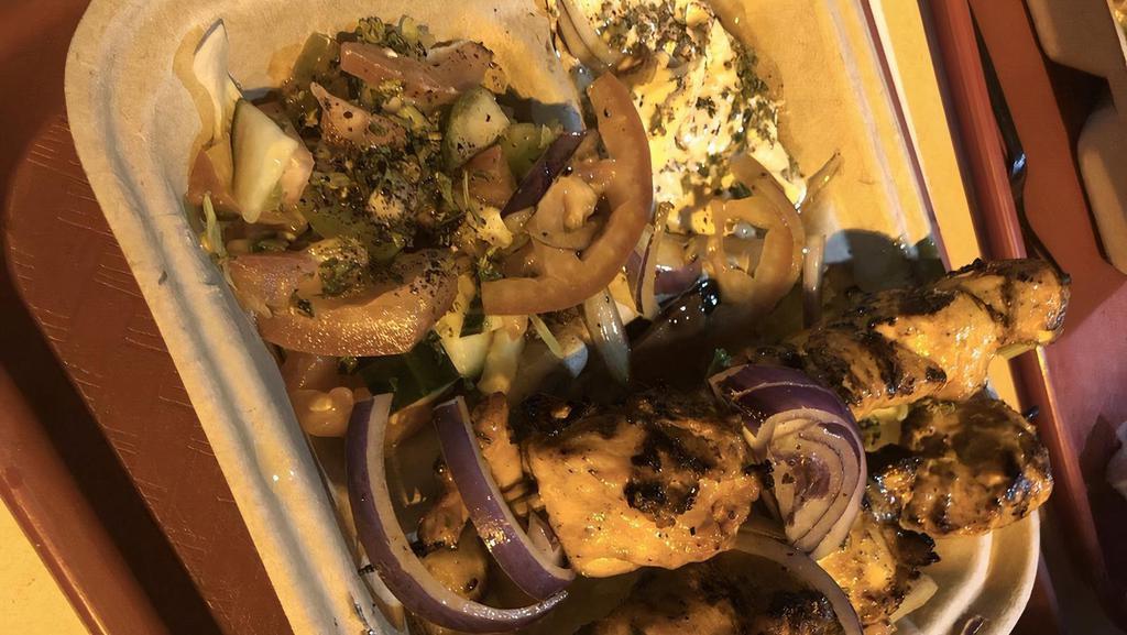 Chicken Kabobs · Two skewers of marinated cubes of chicken shawarma, topped with grilled onions and tomatoes over basmati saffron rice with whole cumin seeds, served with hummus, Mediterranean salad and homemade pita bread.