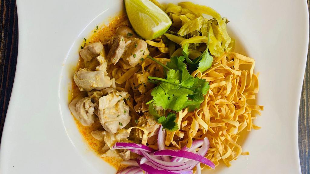 Khao Soi · A curry noodle dish from northern Thailand.  Coconut curry base with chicken, egg noodle, cilantro, pickle, shallot, and lime