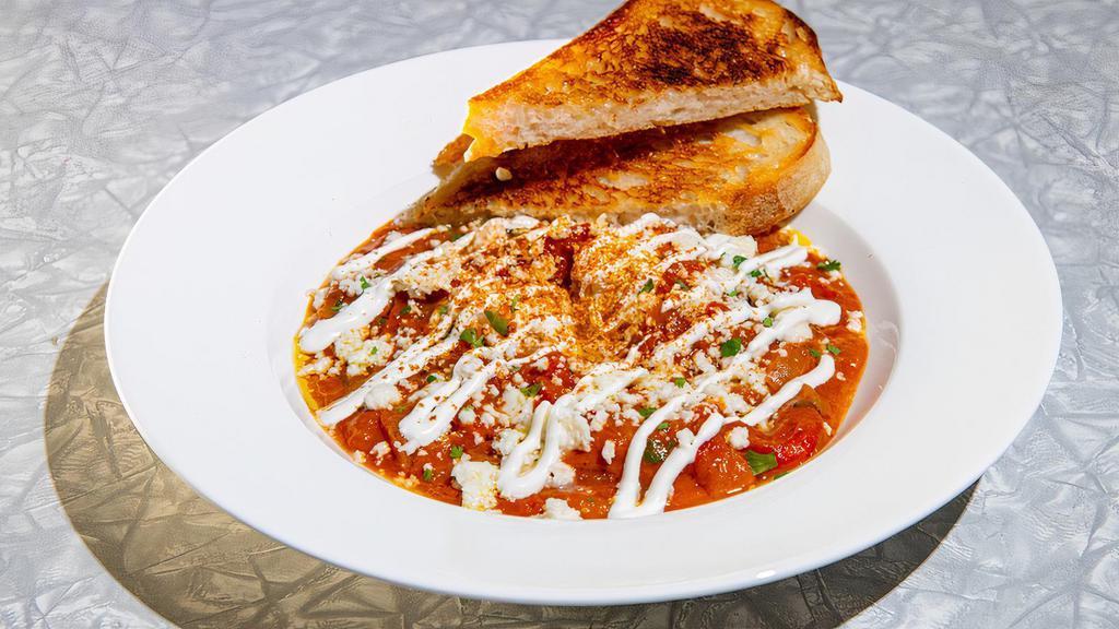 Shakshuka · Two Poached Eggs, Spicy Tomato Sauce, Crema, Roasted Red Peppers, Caramelized Onions, Crumbled Cheese and Herbs served with Grilled Artisan Bread