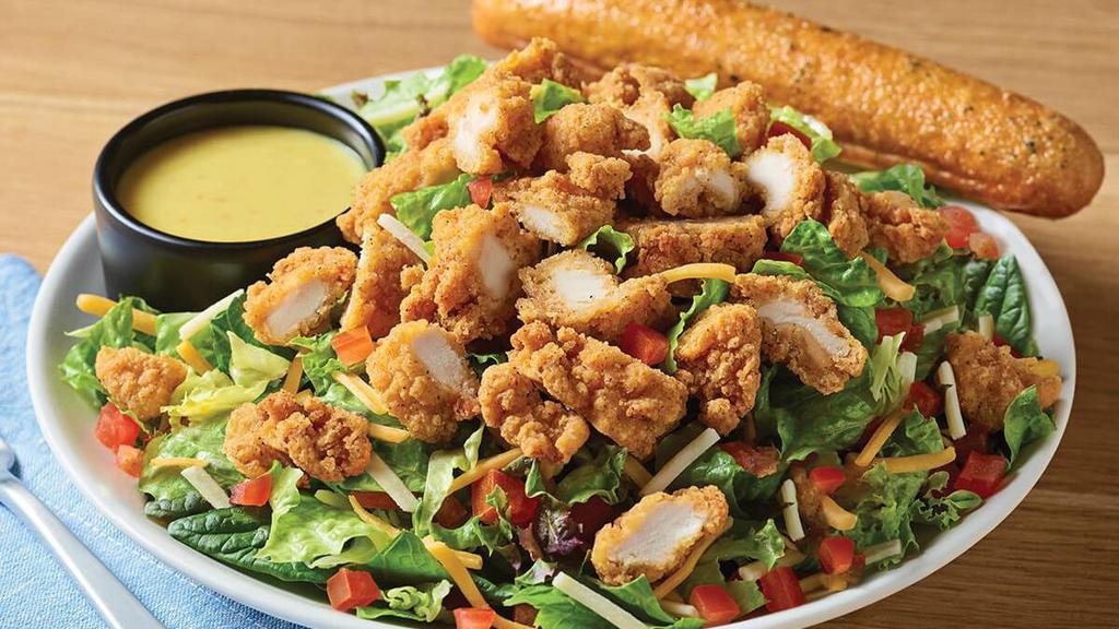 Crispy Chicken Tender Salad · A hearty salad with crispy chicken tenders on a bed of fresh greens topped with a blend of Cheddar cheeses and tomatoes. Served with honey Dijon mustard dressing on the side and a golden brown signature breadstick brushed with buttery garlic and parsley.