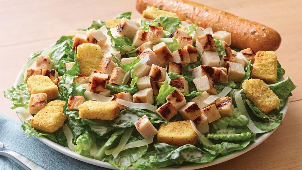 Grilled Chicken Caesar Salad · Crisp romaine tossed in garlic Caesar dressing topped with grilled chicken, croutons and shaved Parmesan. Served with a golden brown signature breadstick brushed with buttery garlic and parsley.