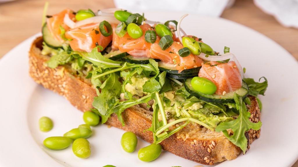 Toast-ess With The Mostest · Toast, Sesame Miso Spread, Hass Avocado, Baby Arugula, Salmon, Cucumber, Green Onions, White Onions, Wasabi Citrus Sauce, Edamame beans, and Furikake.
