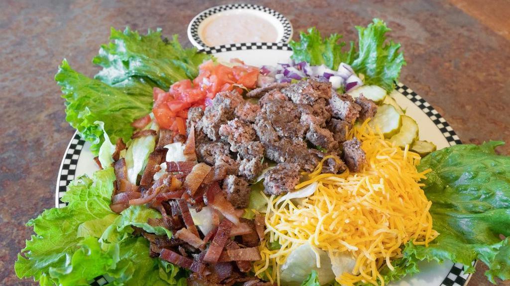 Bacon Cheeseburger Salad · All that’s missing is the bun in this perfect protein-style meal. Salad mix topped with a chopped burger patty*, bacon, dill pickle, tomato, red onion, cheddar cheese & served with Thousand Island dressing..