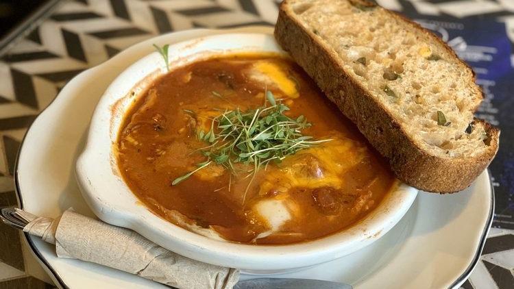 Spicy Baked Eggs · Two eggs, spicy tomato and black bean stew, cheddar, cilantro, olive toast.