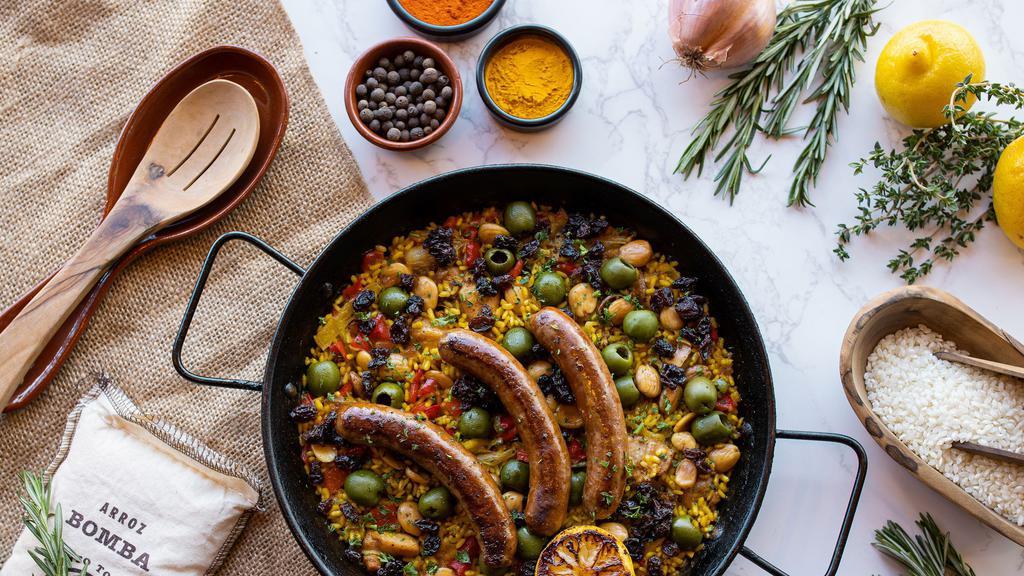 Paella Marroquí · harissa chicken, merguez sausage, almonds, raisins, olives, tomato-onion sofrito, saffron, bomba rice