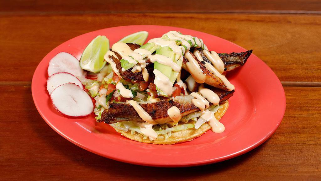 Fish Taco · Grilled fresh fish marinated in garlic, served on a corn tortilla topped with lettuce, salsa fresca, sliced avocado and a spicy chipotle sauce.