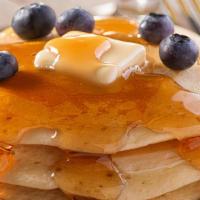 The Blueberry Buttermilk Pancakes · Three pieces of fluffy buttermilk pancakes topped with fresh blueberries, served with butter...