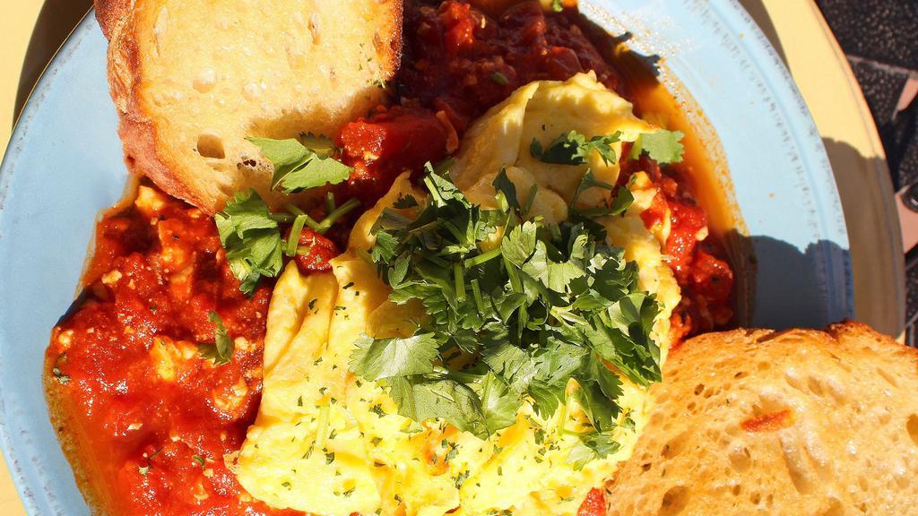 Shakshouka · Two scrambled or fried eggs on a spicy thick sauce of stewed tomatoes, onions, red peppers, garlic & extra virgin olive oil. Topped with crumbled feta & cilantro, served with rustic sourdough.