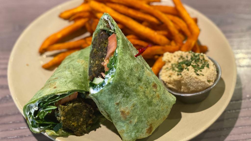 Falafel Wrap · Delicious falafel balls, avocado, pickles, arugula, tomatoes, cucumbers & labneh (mediterranean creamy cheese), wrapped in a spinach tortilla. Served with a choice of side & a choice of dip.