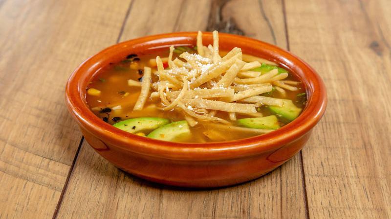 Housemade Tortilla Soup · A bowl of rich chicken broth with diced onion, tomatoes, roasted corn, jalapeños, grilled chicken, crispy tortilla strips, cotija cheese and fresh Haas avocado.