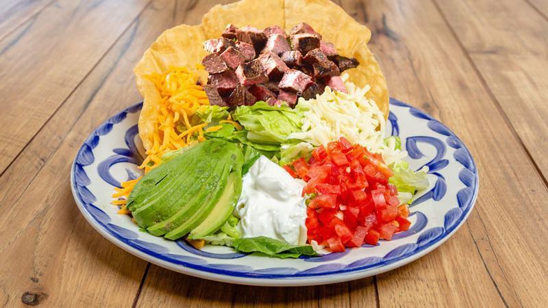 STEAK TOSTADA SALAD · Crispy tortilla shell filled with mesquite-grilled steak, refried beans, romaine, jack & cheddar cheese, avocado and sour cream and our apple-chipotle vinaigrette.