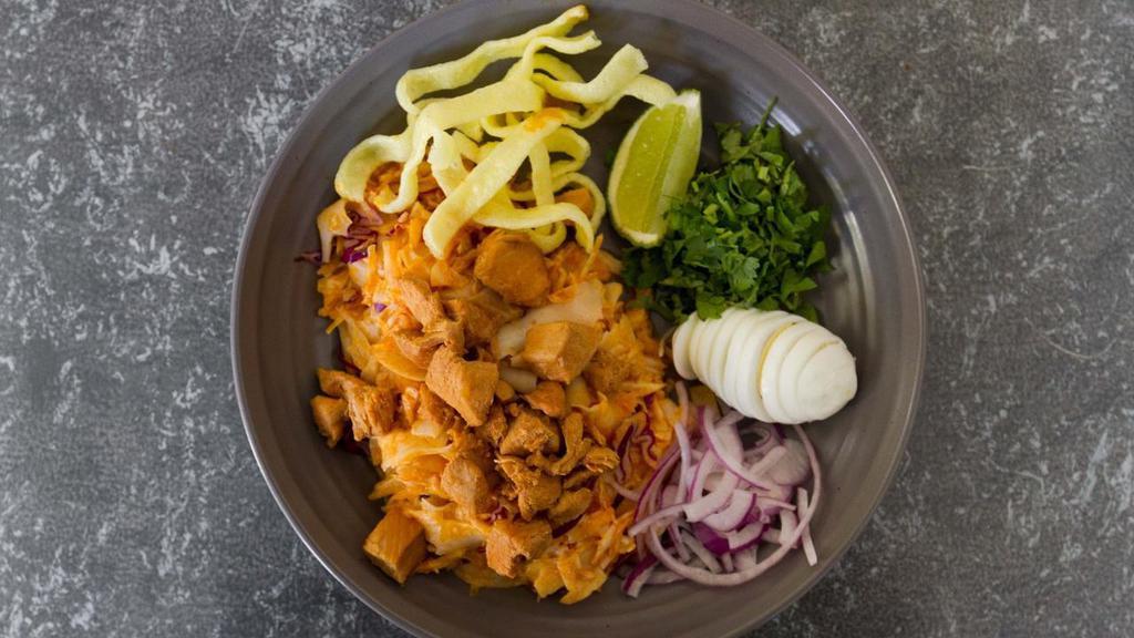 Nan Pya Noodle Salad · Flat flour noodle salad made with small cubed chicken breast marinated in curry sauce. Tossed with julienned cabbage, lime juice, chickpea bean powder & fish sauce. Topped with cilantro, sliced broiled egg, lime, sliced red onions & crispy rice noodles. Served warm.