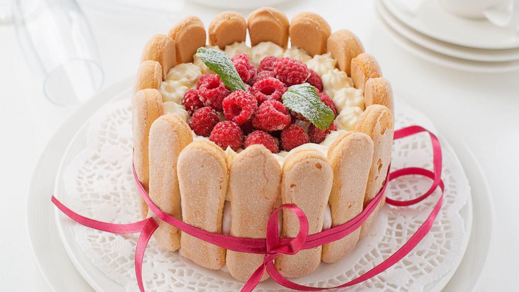 Raspberry Charlotte · Fresh white cake layered with raspberry jam and seedless raspberry cream filling garnished with fresh raspberries and white chocolate shavings.