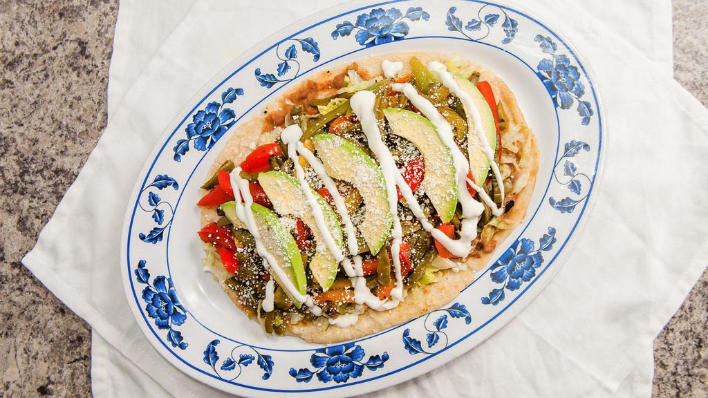 Huarache Mexicano · Eight inch corn flour oval base topped with refried beans, sautéed nopalitos (Mexican cactus), bell peppers and onions, lettuce, fresh avocado, and Cotija cheese.