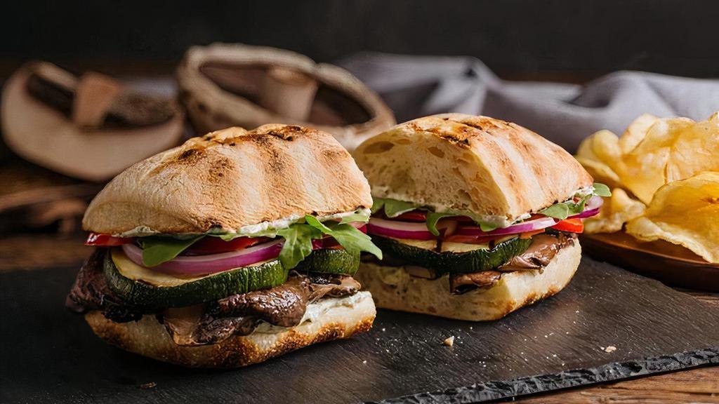 Grilled Portobello Mushroom Sandwich · marinated grilled portobello mushroom, pesto goat cheese, grilled zucchini, julienne red bell peppers, shaved red onion, arugula served on a toasted bun with chips
