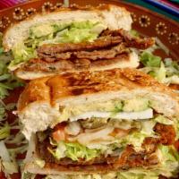 Torta de Milanesa · Toasted bread with a breaded slice of beef, beans, lettuce, onions, tomatoes, jalapeños, sli...