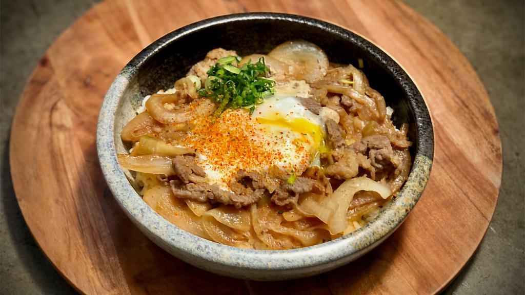 Gyudon · Steamed rice topped with sliced beef and onion simmered in dashi and soy sauce broth, topped with a soft poached egg, green onion, and sprinkle with togarashi chili pepper.