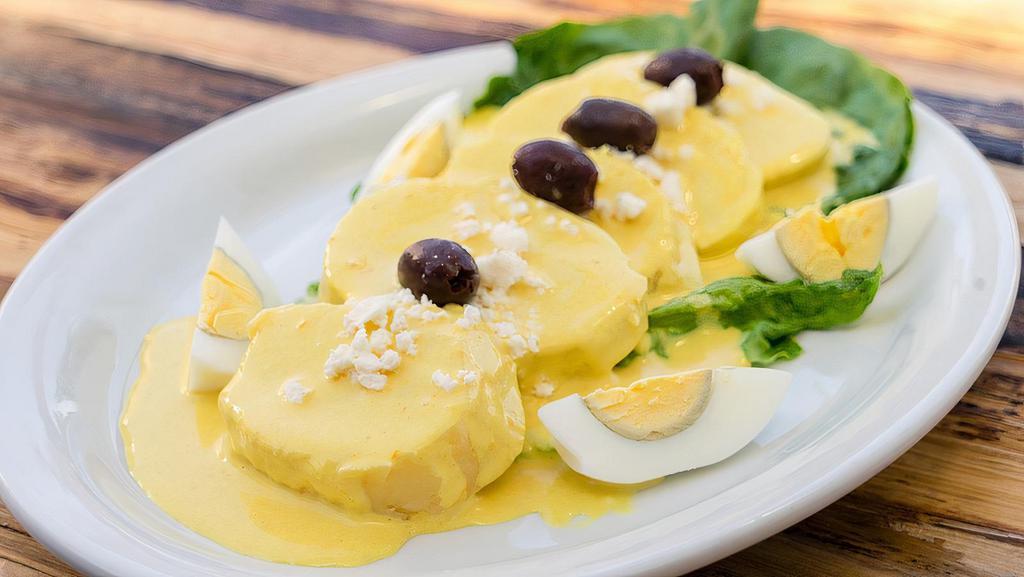 Papita a la Huancaina · Slices of boiled potatoes topped with Aji Amarillo chili and cheese sauce, garnished with Queso Fresco and olives.