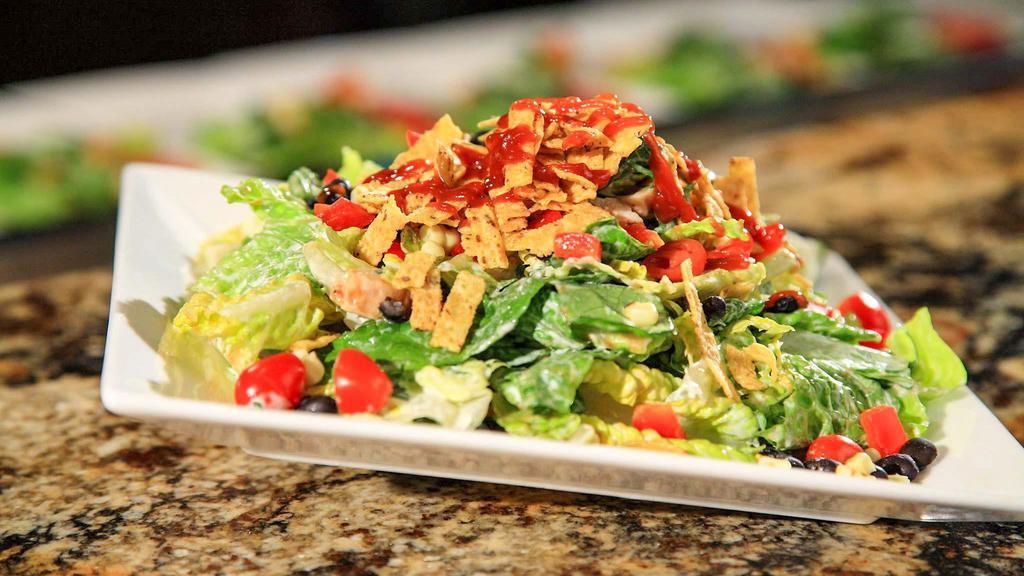 BBQ Chicken Salad · Hand-tossed hearts of romaine with ranch dressing, tortilla chips, diced tomatoes, corn, chopped red bell peppers, chopped red onions, black beans, and chicken marinated with BBQ sauce. Garnished with cilantro and lime.