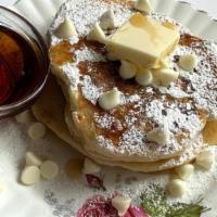 White Chip Buttermilk Pancakes · 2 large buttermilk white chocolate chip pancakes with syrup and butter.