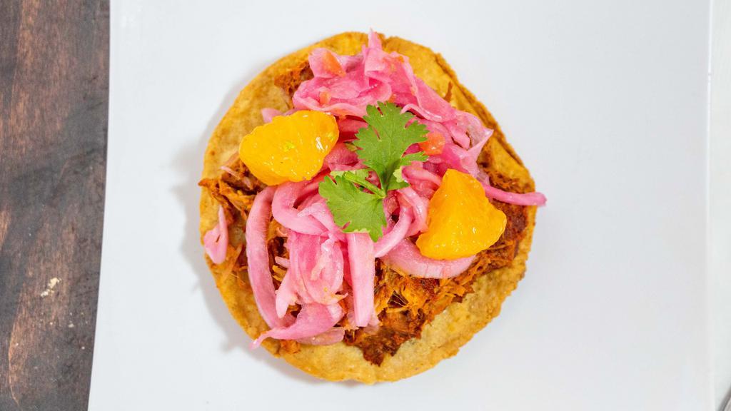 Panucho · Small handmade tostada stuffed with beans, topped with cochinita pibil, red onions with habanero and mandarin wedges.