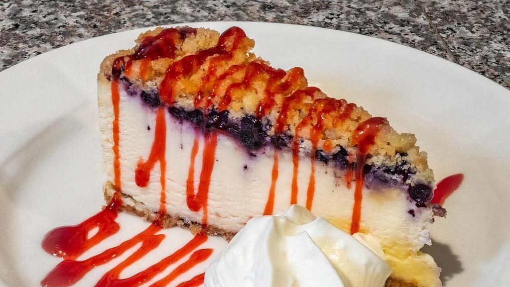 Lemon Blueberry Crumb Cheesecake · A creamy lemon cheesecake topped with blueberries & brown sugar. crumbs sits on a cookie base