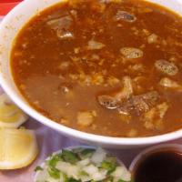 BIRRIA · Goat soup served with lime slices, a side of chopped onions, and salsa.