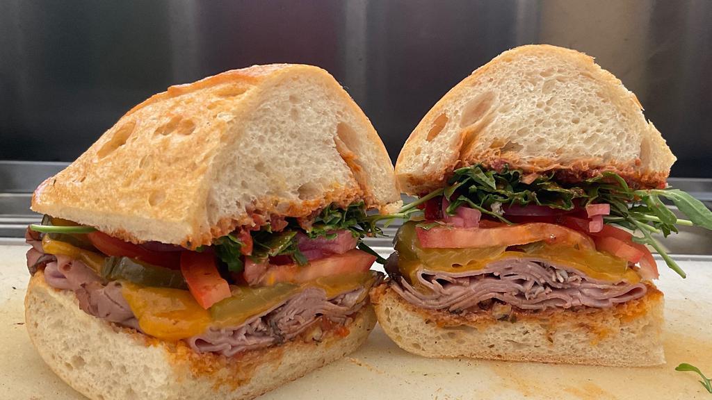 Roast Beef with Walnut Romesco · Roast beef, arugula, tomatoes, red onions, pickles with cheddar cheese and romesco spread on a sourdough roll.