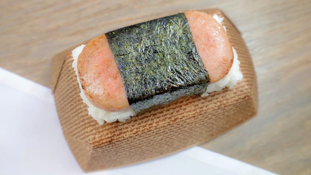 Spam Musubi · A slice of grilled spam on top of a block of rice wrapped together with nori. 
NOTE: We make all musubi's using white steamed rice. There are no substitutions. Sorry!