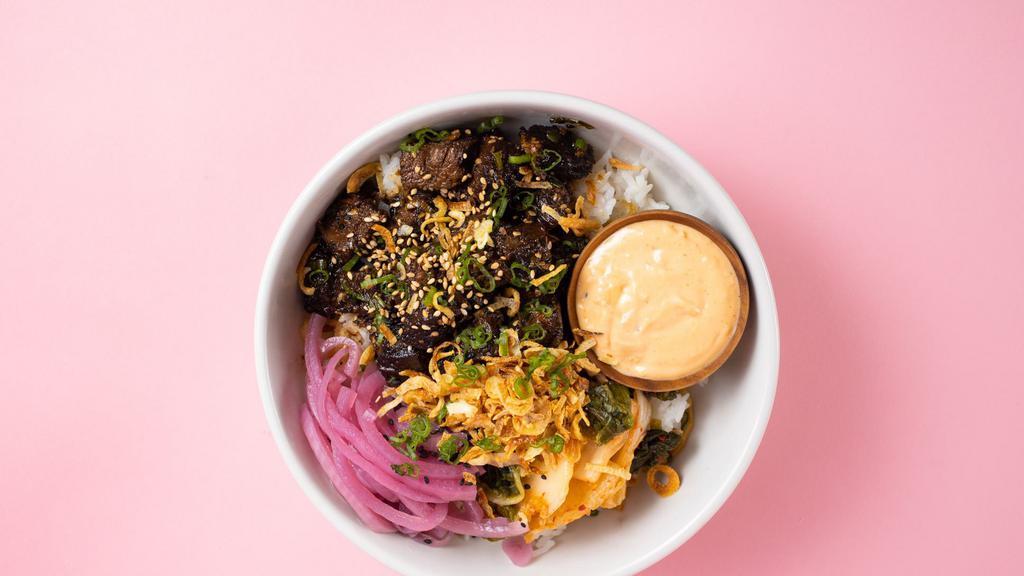 Braised Beef Rice Bowl · Korean braised beef served with garlic sauce, kimchi, green onions and sesame over steamed rice topped with crispy onions.