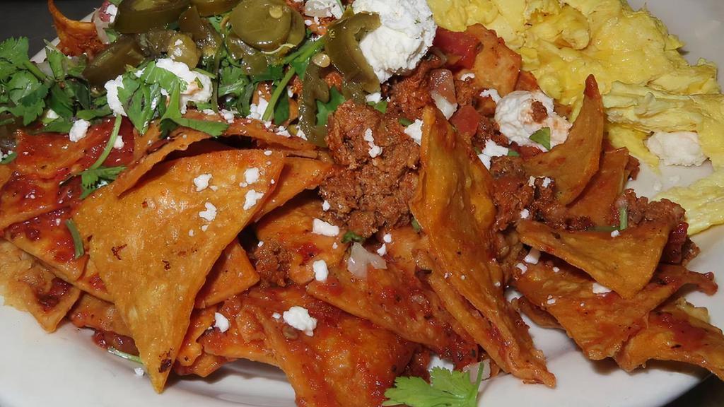 Chilaquiles · Tortilla chips tossed in spicy salsa roja, topped with 2 scrambled eggs, sliced jalapeños, tomato, onions, avocado, queso fresco and cilantro.