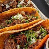 Tacos de Birria · Juicy shredded beef served w/ cilantro, onion, avocado serrano sauce & consommé.