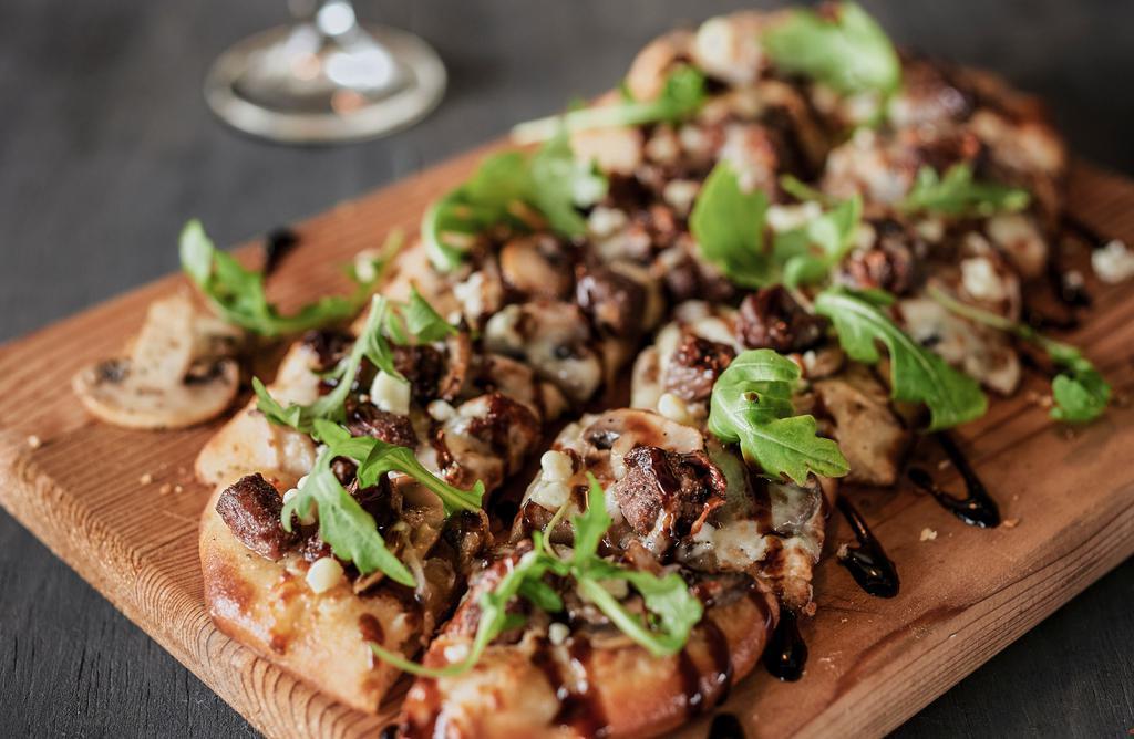 Black & Blue Steak Flatbread · Blackened steak, caramelized onions, and mushrooms, mozzarella and blue cheeses, finished with fresh arugula and a sweet balsamic glaze.