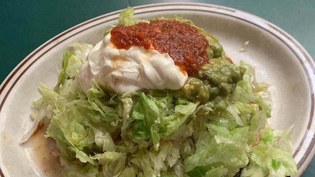 Deluxe Tostada · Choice of beef, picadillo or chicken on a crisp flour tortilla, with beans, melted cheese, topped with lettuce, house red sauce (contains peanut butter) sour cream and guacamole.
