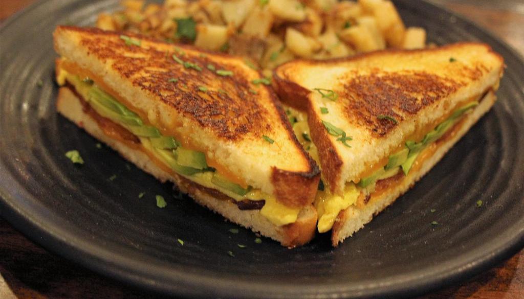 Breakfast Sandwich · WITH SCRAMBLED EGGS, HARDWOOD SMOKED HONEY CURED BACON, AVOCADO AND CHEDDAR CHEESE WITH HOUSE POTATOES ON SLICED WHITE BREAD.