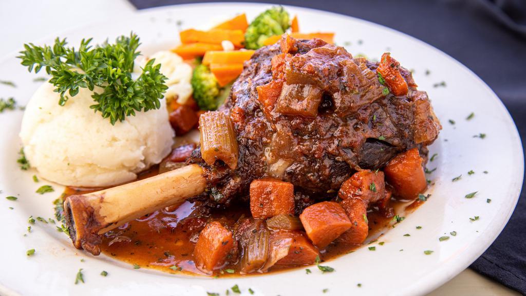Jarret D'agneau · slow-cooked lamb shank with fresh rosemary, garlic, tomatoes & red wine, served with 2 sides.