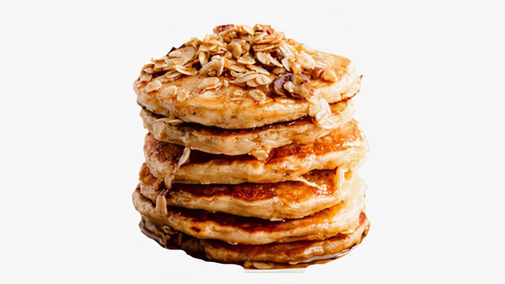 Granola B*tches Pancakes · Two fluffy pancakes topped with granola and served with a side of butter and syrup.