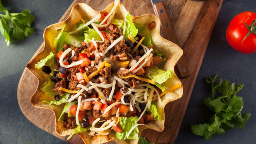 Crispy Taco Salad · Delicious crispy taco salad prepared with fresh romaine lettuce topped with black beans, shredded cheese, salsa fresca and guacamole, served in a crispy tortilla shell.