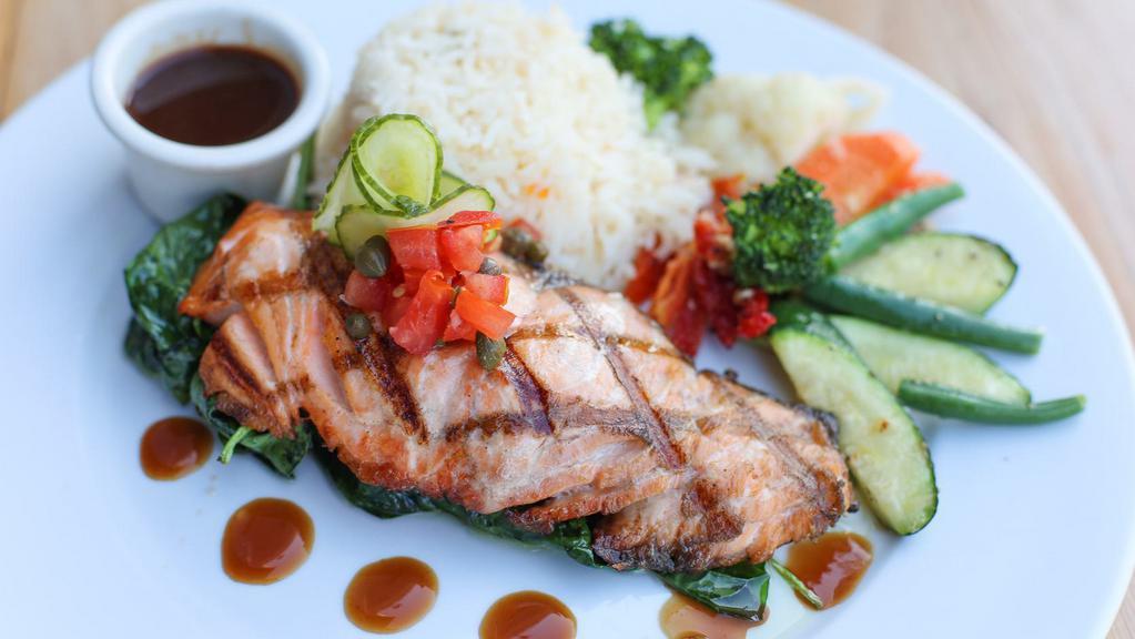 Grilled Atlantic Salmon · served over sautéed spinach with a tarragon port wine sauce and tomato caper salsa, topped with pickled cucumbers, served with a side of vegetables and basmati rice.