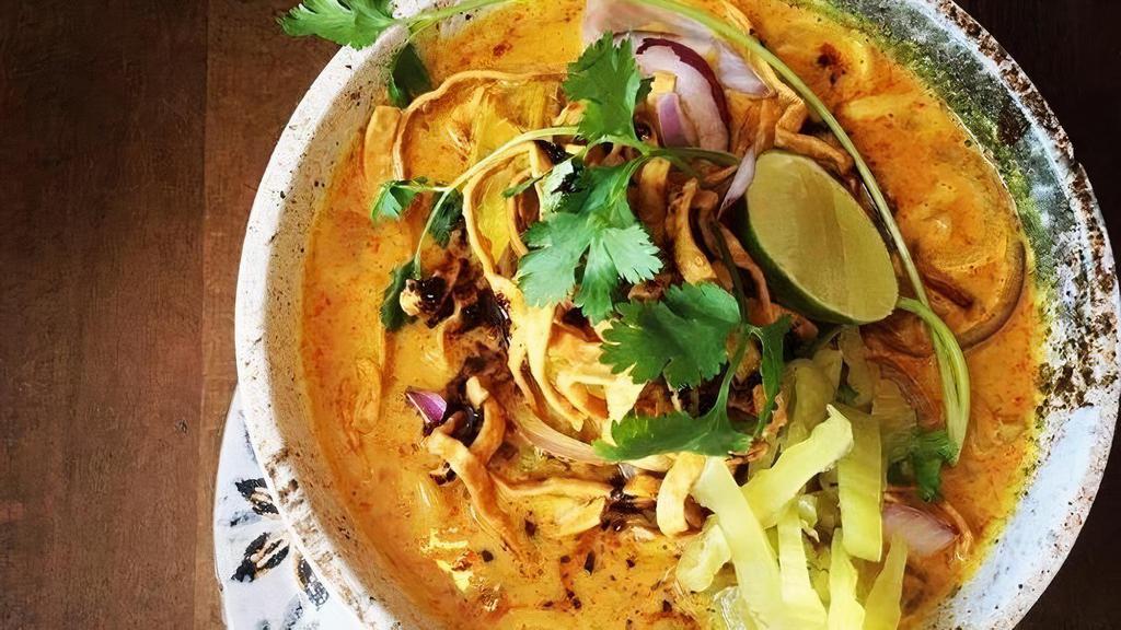Khao Soi · Chicken drumstick with Egg noodles in coconut curry. Lime, red onion, cilantro, and pickled lettuce