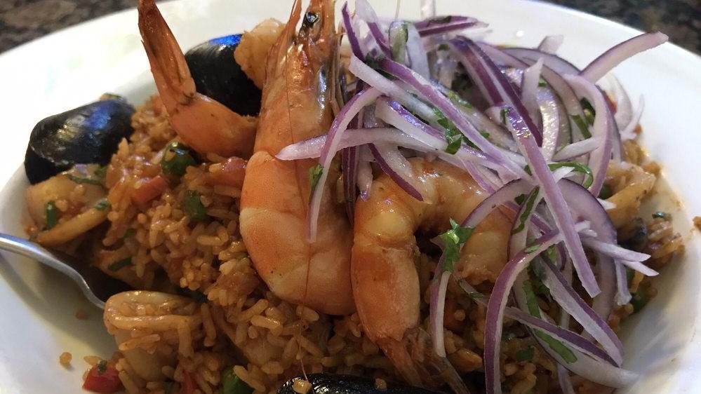 Arroz con Mariscos · Peruvian paella (rice, shrimp, calamari, mussels, aji panca, spices and herbs) served with salsa criolla.