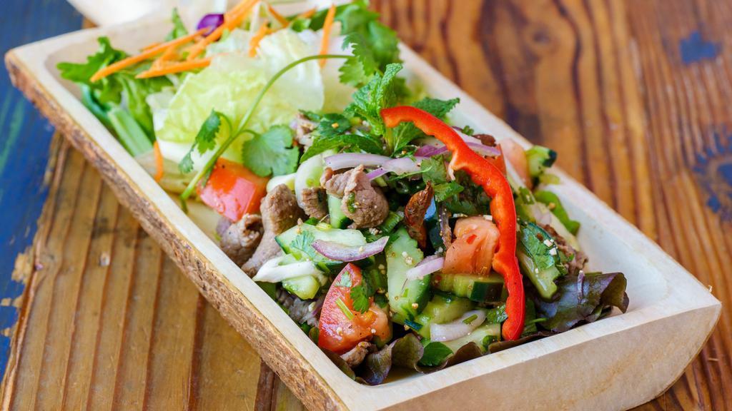 Yum Nua · Grilled slices beef with lemongrass, onions, mint, cucumber, tomato, cilantro, roasted rice seasoned with lime dressing.